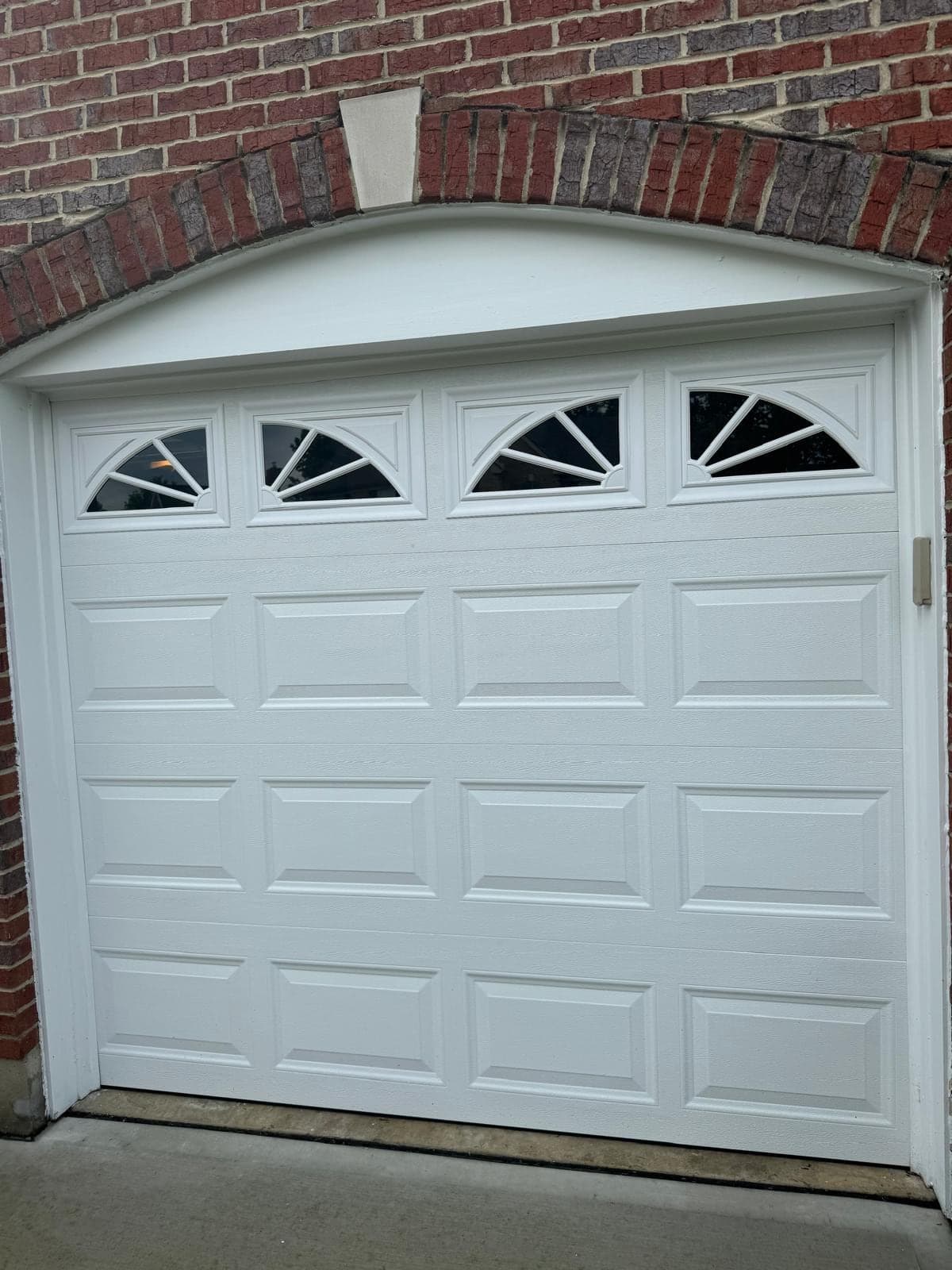 A white raised-panel garage door with four sunburst-pattern windows set under a brick arch